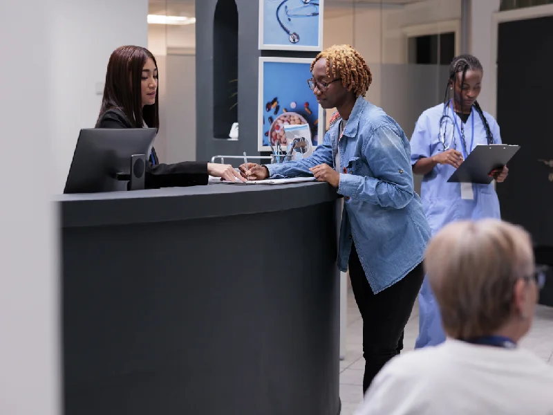 Busy clinic front desk with staff helping patients at the counter