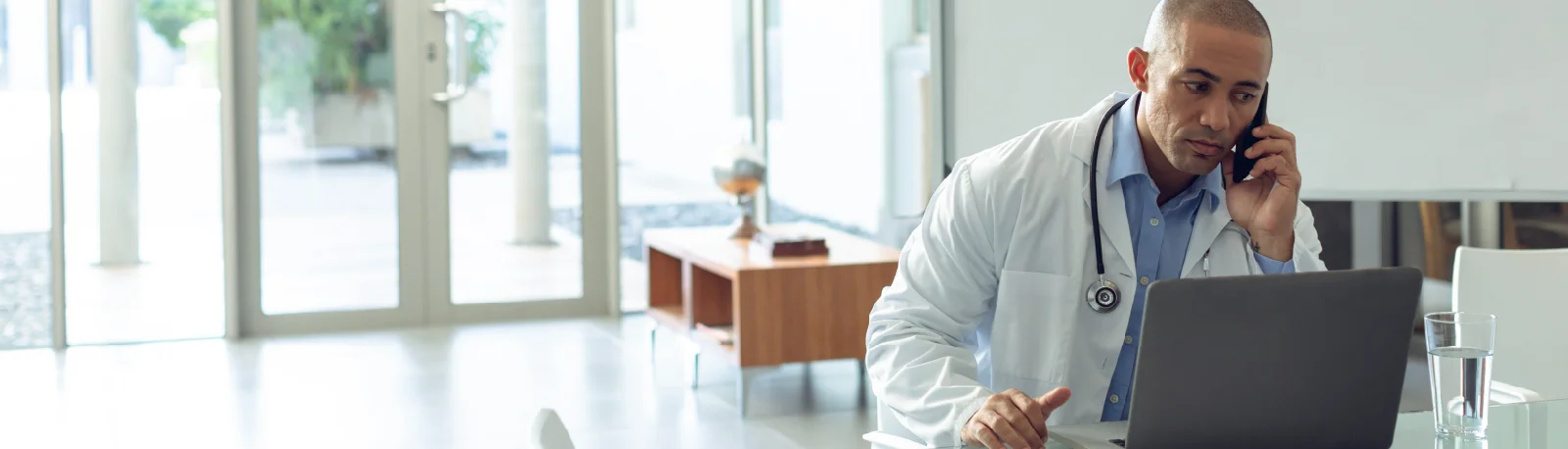 Doctor on a phone call while working on a laptop in a clinic office