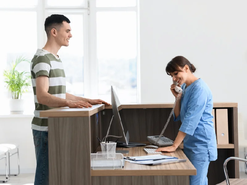 Front-desk staff member answering a phone call while a patient waits at the counter