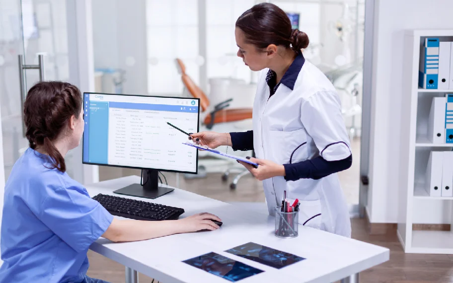 Dental assistant and front-desk coordinator reviewing patient follow-ups on a computer