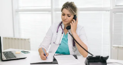 Clinic staff member on a phone call taking notes at a desk