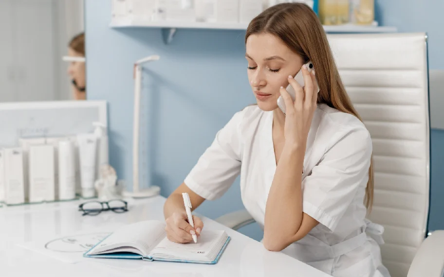 Dental front-desk team member taking a patient phone call and writing notes